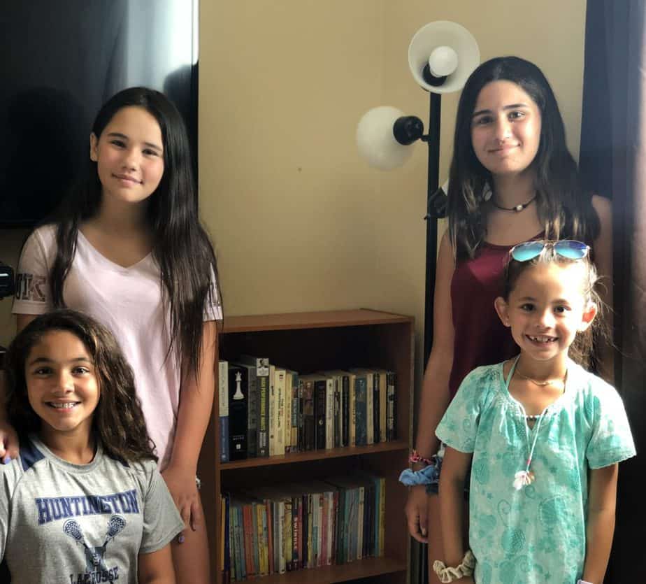 Four children stand with a completed bookshelf, full of donations